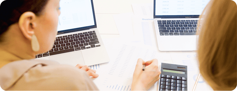 Finance teammates reviewing spreadsheets and charts on laptops with a calculator on the desk