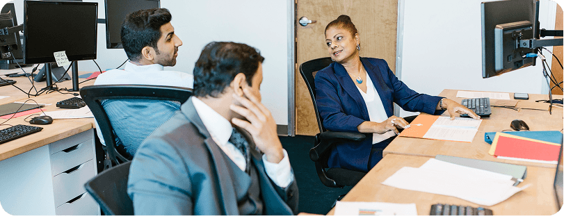 Operations professionals collaborating at desks with dual monitors in a modern open office